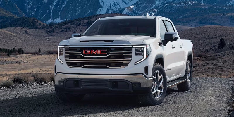White GMC Sierra truck on a dirt road, with mountains and dry brush in the background.