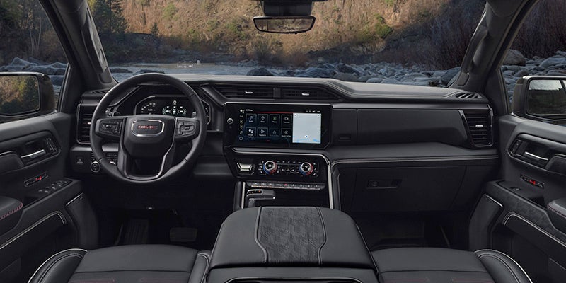 The interior of a GMC truck shows a black dashboard, steering wheel, and seats, with a digital display for the infotainment system.