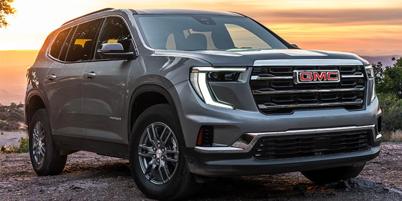 Front view of a gray 2025 GMC Acadia SUV parked outdoors at sunset.