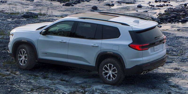 Side and rear view of a 2025 GMC Acadia SUV parked on rocky terrain.
