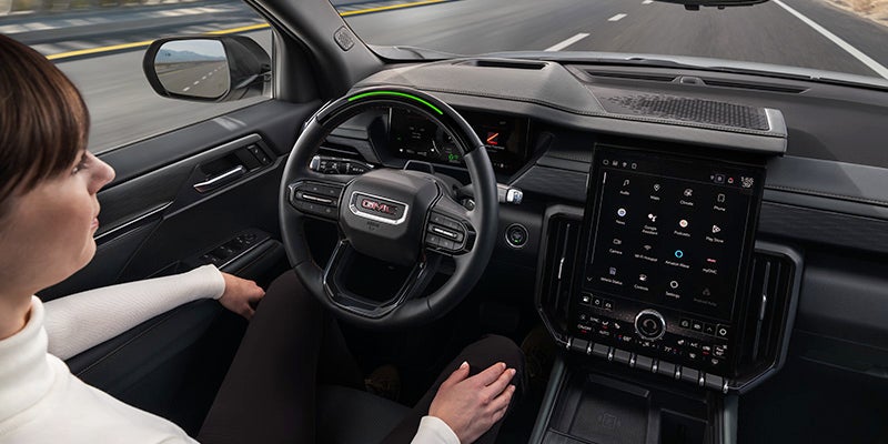Interior view of the 2025 GMC Acadia showing the driver seat, steering wheel, and touchscreen display.