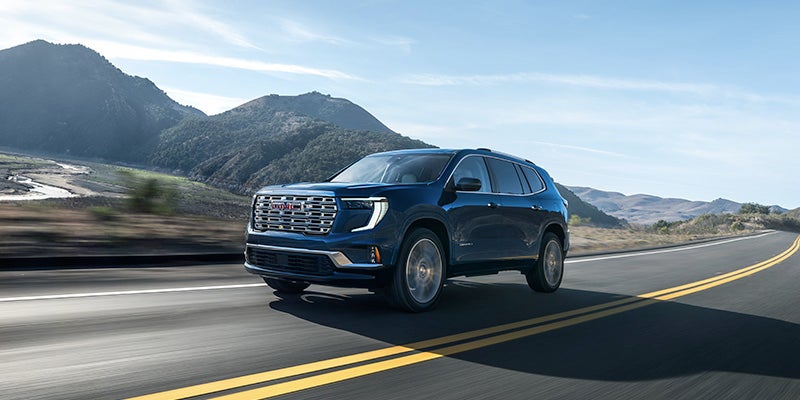 2025 GMC Acadia driving on a highway with mountains in the background