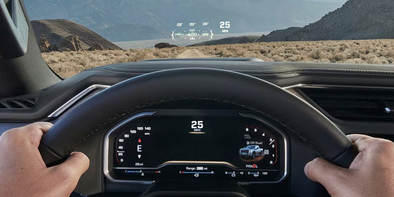 A driver's view from inside a vehicle, dashboard and gauges in foreground, desert landscape through windshield, heads-up display showing 25 mph.
